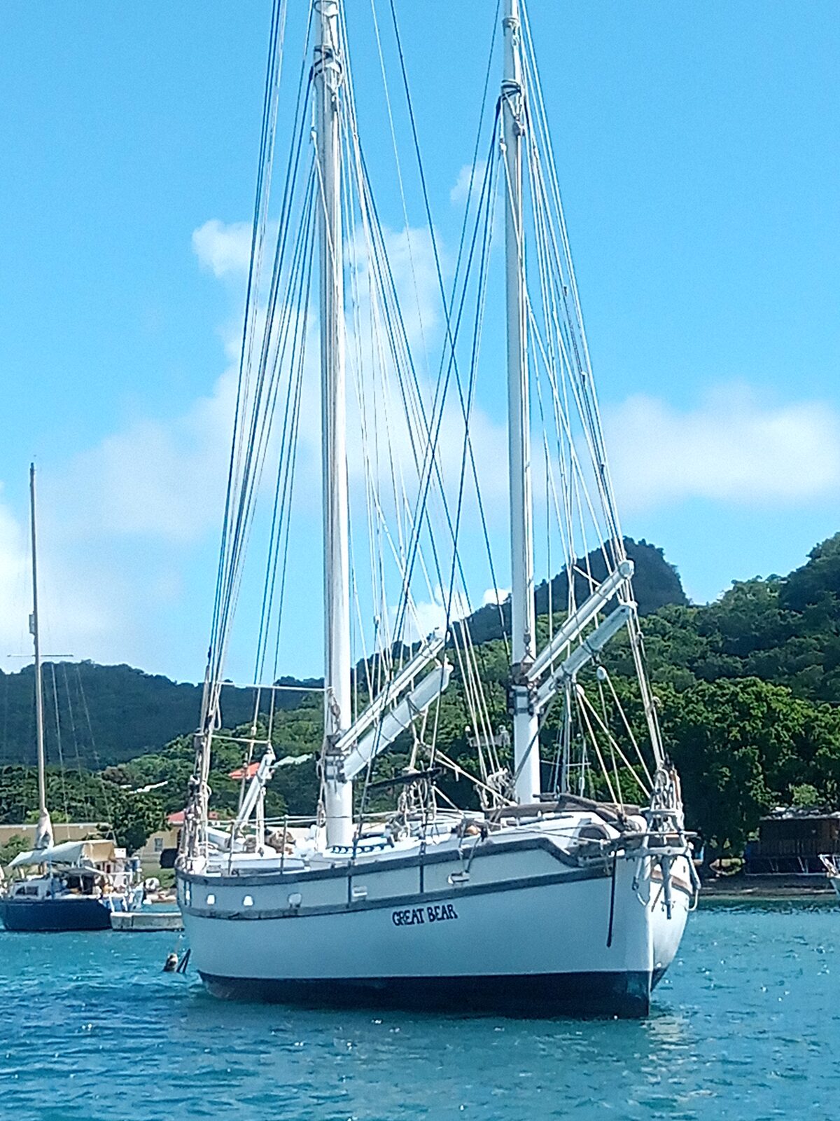 Cherub lying quietly at anchor in a calm bay beneath a green peak